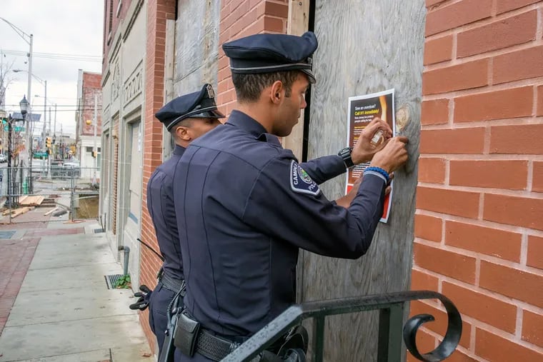 Camden County Officers Vidal Rivera (left) and Tyrell Bagby post information on a boarded-up building on Broadway. They were part of the outreach effort.