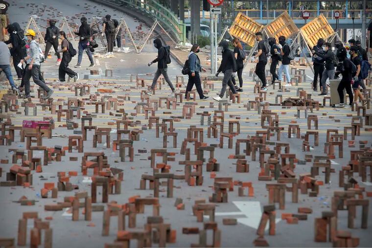 Protesters walk past barricades of bricks on a road near the Hong Kong Polytechnic University in Hong Kong, Thursday, Nov. 14, 2019. Hong Kong residents endured a fourth day of traffic snarls and mass transit disruptions Thursday as protesters closed some main roads and rail networks while police skirmished with militant students at major universities.