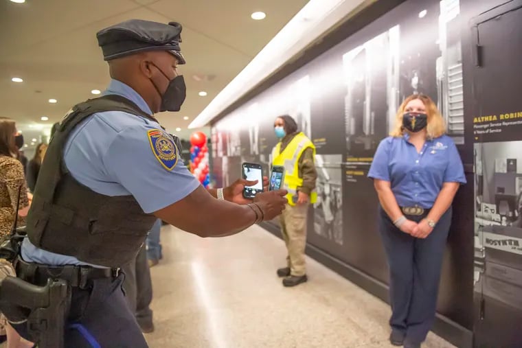 Officer Gary Miller photographs Althea Robinson, a passenger service representative, next to her name on the wall. On Thursday, SEPTA workers and management gathered in Suburban Station for the unveiling a tribute wall honoring its frontline employees.