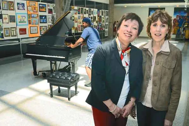 Virginia Lam (left), who began as a music teacher 37 years ago and her best friend, Tessie Varthas, who developed the district's art competition pose in atrium of the School District administration building on their last day of work June 28, 2013. Moving the baby grand piano is Jason Rodgers, who is currently the assistiant conductor with the Black Pearl Chamber Orchestra (on his way to conduct at a festival in Italy). He took his first piano lessons with Lam when he was in the 8th grade. The art work on walls is from the annual student art competition. ( TOM GRALISH / Staff Photographer )