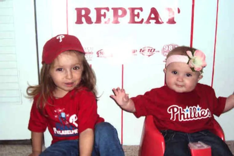 Grace Walsh (left), 2, and sis Finnley, 7 months, discussed their hopes for a Phillies win in their Havertown basement recently. Both agreed they did not want to wait another 28 years for a championship. Parents Jen and Dan Walsh, lifelong Phillies phanatics, agree.