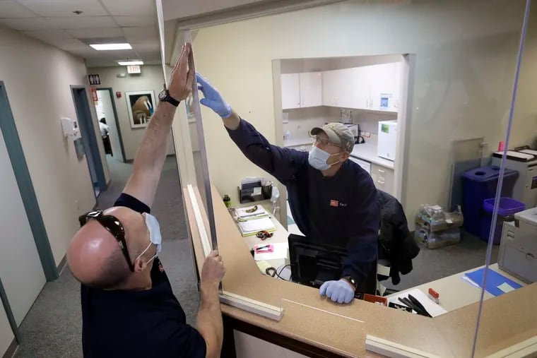 In this May 20, 2020 photo carpenters John Mackie, of Canton, Mass., left, and Doug Hathaway, of Holliston, Mass., right, apply trim to a newly installed plastic barrier in an office area, at Boston University, in Boston. Boston University is among a growing number of universities making plans to bring students back to campus this fall, but with new measures meant to keep the coronavirus at bay. (AP Photo/Steven Senne)