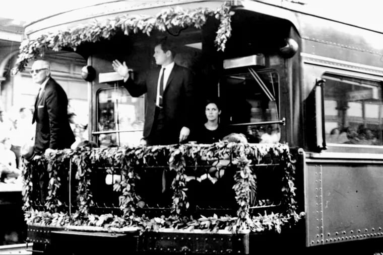 Sen. Edward M. Kennedy waves from the rear platform of the observation car bearing the remains of his slain brother, Sen. Robert F. Kennedy, as the funeral train passed through North Philadelphia Station, June 8, 1968. Others on platform are unidentified. 