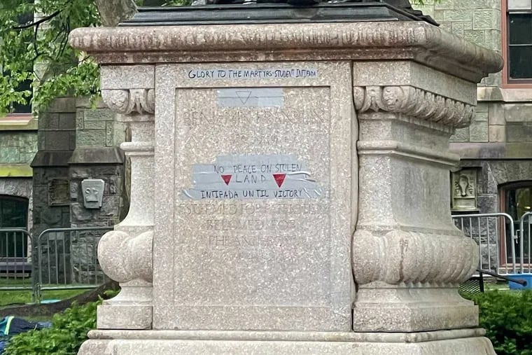 Grey tape with red triangle markings and text on the base of the Ben Franklin statue at University of Pennsylvania, in Philadelphia, Friday, May 10, 2024.