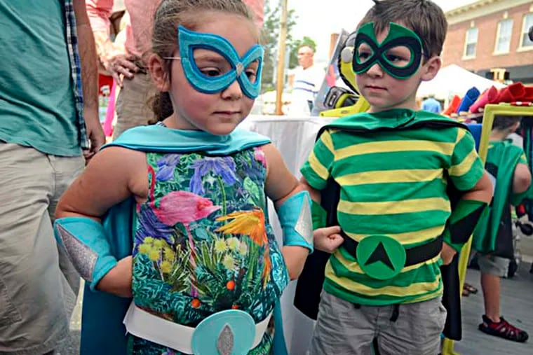 Joey McGinley (right), 5, and his sister Annah McGinley (left), 3-1/2, look at themselves in the mirror while picking out their colors and style of superhero capes from Creative Capes ("with premium satin featuring your child's first initial") while shopping July 13, 2014 at the annual Haddonfield Crafts and Fine Art Festival with their dads, Martin and Steve McGinley of Haddon Township. ( TOM GRALISH / Staff Photographer )