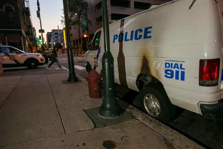 Philadelphia police officers sit on a police van parked on the southwest corner of S. 7th and Chestnut Streets. Overnight, several police vehicles suffered fire damage.