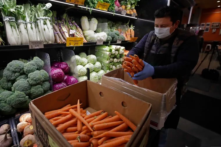 A worker, wearing a protective mask against the coronavirus, stocks produce before the opening of Gus's Community Market, Friday, March 27, 2020, in San Francisco. (AP Photo/Ben Margot)