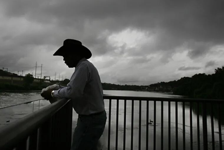 Under a menacing sky, Robert Jones of Philadelphia fed fish yesterday in the Schuylkill near the Water Works. Though the trend may be ending, this summer has brought a string of sub-70 lows unlike any in the region since 1963. (Eric Mencher / Staff Photographer)
