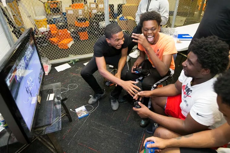 Frankford football players (from left) Kelly Battis, Hadiya Ba, and Baxter Peterson play a video game in their team's locker room last week. Their coach, Bill Sytsma, invites his players to spend Friday nights together in the locker room during the spring and summer months to avoid trouble on the streets.