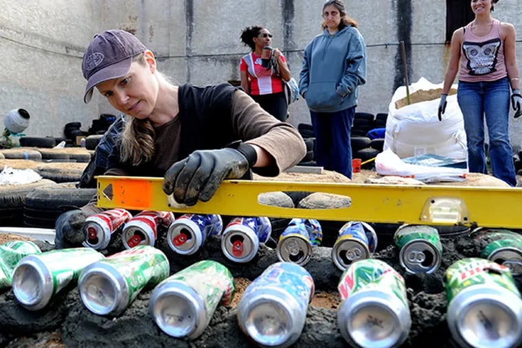 Kristin Mitchell, of West Chester, uses a level to adjust aluminum cans that are being set in cement on top of tires as part of a wall for an Earthship House being built on the 600 block of North 41st Street. ( CLEM MURRAY / Staff Photographer )