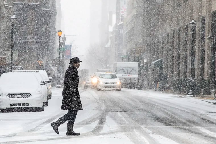 A pedestrian crosses the street in Center City during a February snowfall. Computers had anticipated significant snow this week, and then said: nevermind.