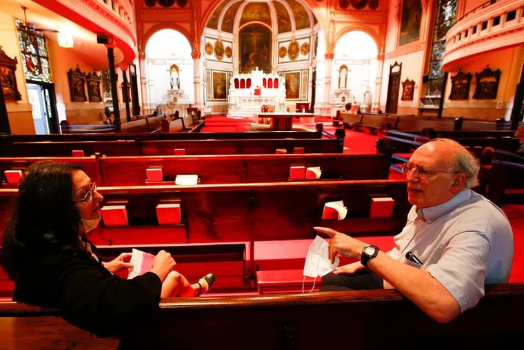 Donna Panno (left) and Stuart Brian talk inside St. Michael's Roman Catholic Church in Olde Kensington. Promised restorations to the church that was altered during its coronavirus shutdown without the consent of its parishioners will have to wait until the sale of another church to pay for them, an Archdiocese representative told church members Sunday.