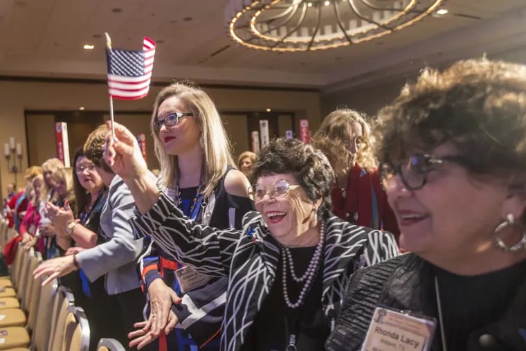 Juandelle Roberts, center, from Midland, Texas, waves her American flag as she, the Texas delegation, and the entire general assembly give Carrie Almond, the president of the National Federation of Republican Women, a standing ovation at the beginning of the general session on Sunday in Philadelphia.