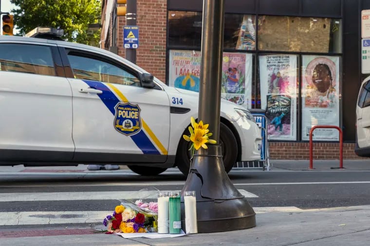 A Philadelphia police officer patrol car rolls past a makeshift memorial to the victims of Saturday evening's mass shooting along South Street.