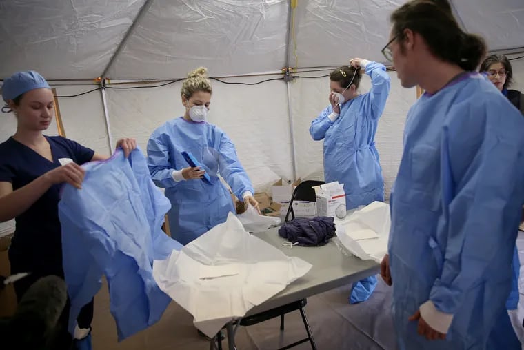 Philadelphia Medical Reserve Corps volunteers (from left) Jamie Huot, Marina Spitkovskaya, Megan Boyle, and Stephen Bonett, all of whom are nurses, put on their protective equipment as the city's coronavirus testing site prepared to open next to Citizens Bank Park on March 20.