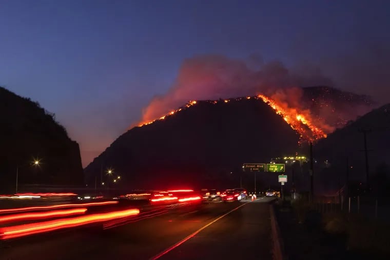 Traffic continues as flames roar up a steep hillside near the Getty Center in Los Angeles. The blaze forced evacuations and has burned more than 600 acres.