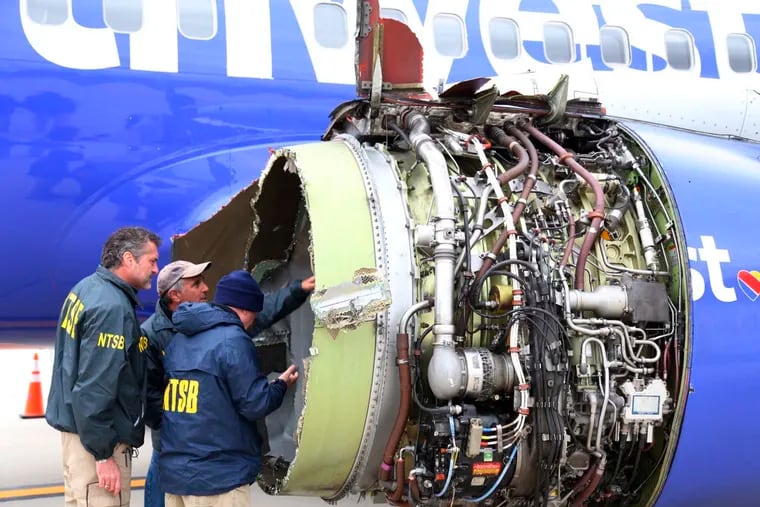 FILE- In this April 17, 2018, file photo National Transportation Safety Board investigators examine damage to the engine of the Southwest Airlines plane that made an emergency landing at Philadelphia International Airport in Philadelphia. In new accounts released Wednesday, Nov. 14, into the April accident, the flight attendants described being unable to bring the woman back in the plane until two male passengers stepped in to help. The flight attendants told investigators at least one of the men put his arm out of the window and wrapped it around the woman's shoulder to help pull her back in.