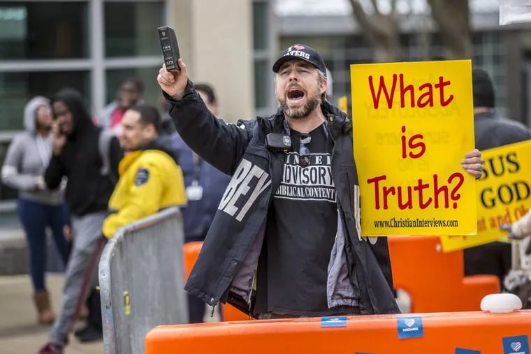 Holding a sign and a bible, pastor Aden Rusfeldt of the Key to David Church, yells at passing students in the quad of the Community College of Philadelphia on March 26, 2018.