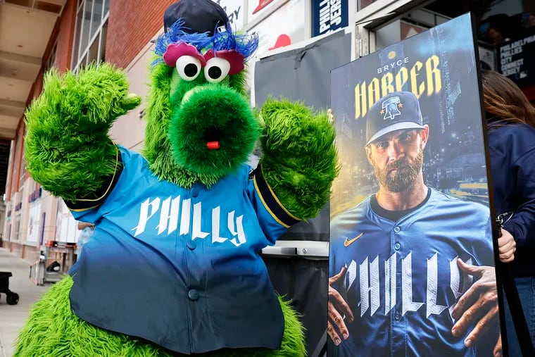 The Phillie Phanatic shows off the Phillies' City Connect jersey next to a photo of Phillies first baseman Bryce Harper. The team will debut their new look tonight.