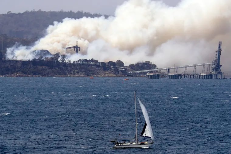 A yacht sails past a burning woodchip mill as the wildfires hits the town of Eden, New South Wales, Australia, Friday, Jan. 10, 2020. The wildfires have destroyed more than 2,000 homes and continue to burn, threatening to flare up again as temperatures rise.