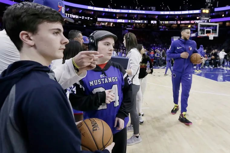 As Sixers player Ben Simmons warms up next to them, Johnny Burke (left) and his brother Tony Burke receive instructions before delivering the game basketball prior to the Brooklyn Nets vs. Phila. 76ers NBA game at the Wells Fargo Center in Phila., Pa. on March 28, 2019.