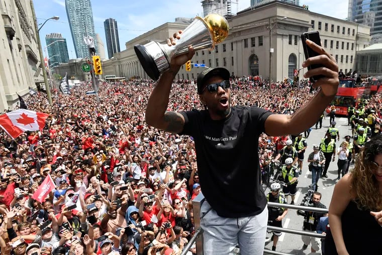 Kawhi Leonard taking a selfie while holding his playoff MVP trophy during the Raptors' championship parade Monday.