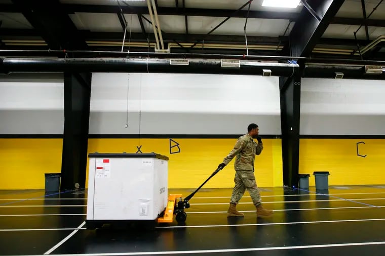 A member of the 103rd Brigade Engineer Battalion National Guard moves a box full of supplies in the gymnasium at the Glen Mills School March 28. FEMA and National Guard members will assemble medical equipment and beds in the field hospital to make room for coronavirus patients elsewhere.