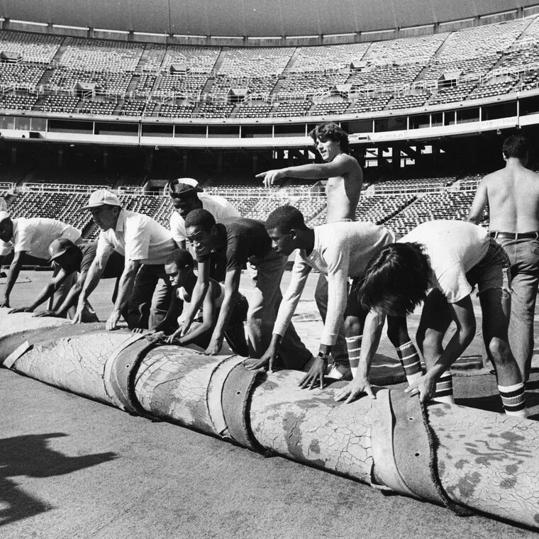 Grounds crew take up the AstroTurf at third base in Veterans Stadium to convert the field from football to baseball on Aug. 1, 1981.
