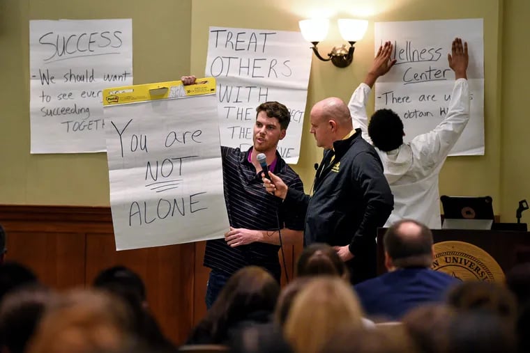 Physical education major Austin Gillis (left) uses oversize post-it notes as he speaks during a Rowan University forum to talk about recent campus suicides Dec. 9. Advertising major Justice Lateef (right) posts the notes on the wall as Scott Woodside, the university's Wellness Center Director of Student Health Services, holds the microphone.
