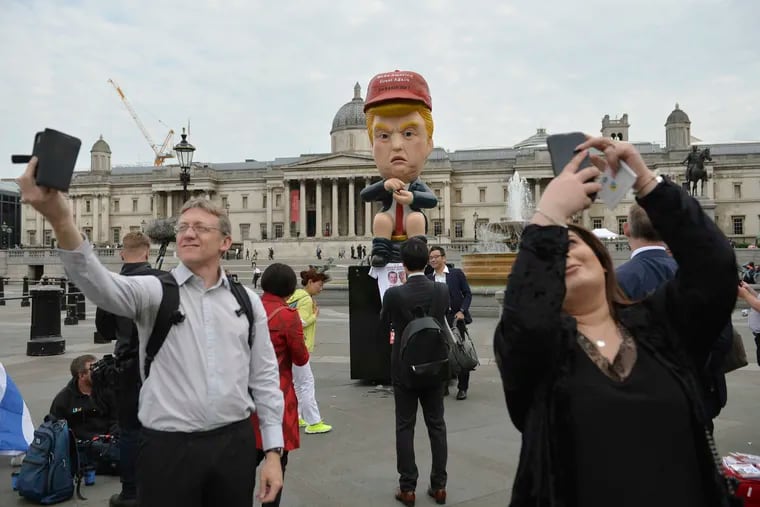 Commuters and tourists take selfies backdropped by a 16-foot talking robot depicting US President Donald Trump sitting on a gold toilet in Trafalgar Square, London, on Tuesday June 4, 2019.  Some protest groups are using the State Visit to the UK to demonstrate against various issues. The National Gallery is in the background. (Jacob King/PA via AP)