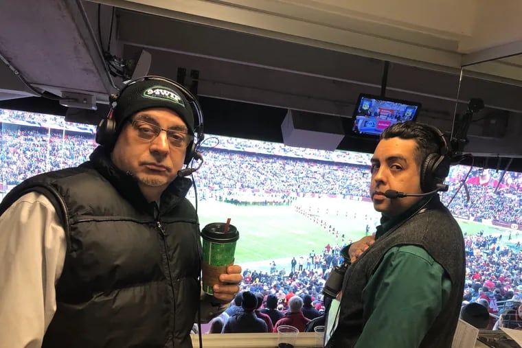 Rickie Ricardo (left) stands next to sports analyst Gustavo Salazar in the broadcasting booth during the national anthem at an Eagles game.