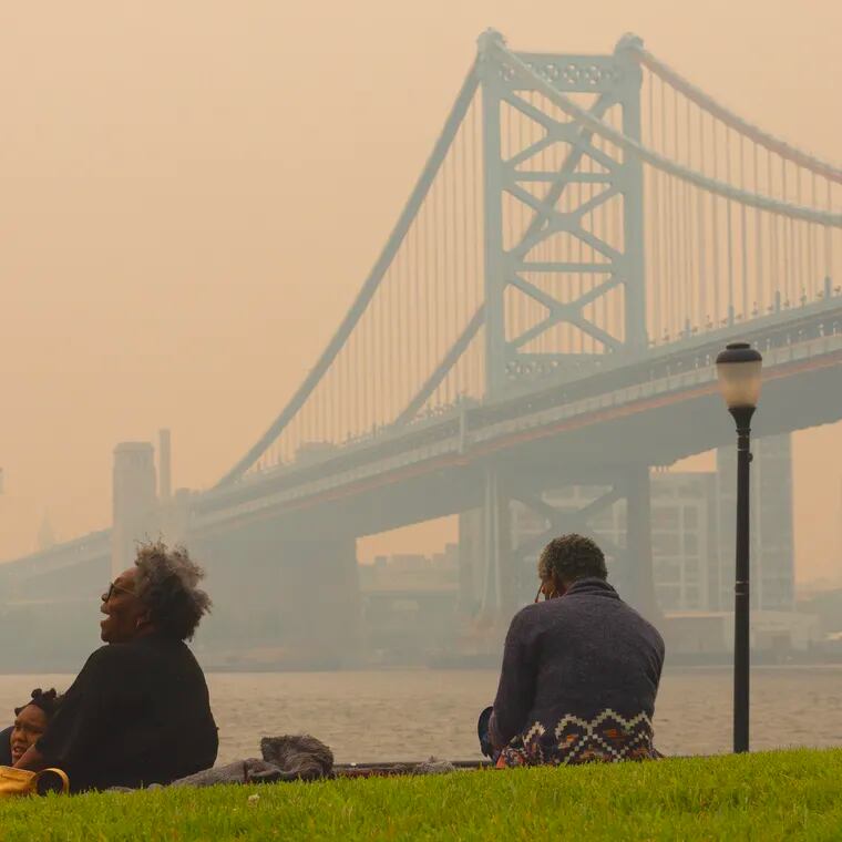 The Jackson family from Pennsauken sits along the Camden waterfront with Philadelphia and the Ben Franklin Bridge in a smoky haze in the background  on June 7.