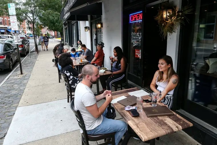 On Main Street in Manayunk, Ryan Monte and Stephanie Santamaria dine outdoors at the New Leaf II on Tuesday. The city postponed plans to allow indoor dining that was to begin Friday.