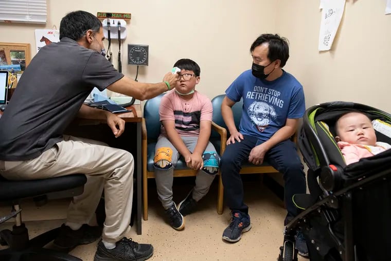 P.J. Parmar examines Johnny Lun Ring at the Mango House clinic in Aurora, Colo., on June 24, 2021. His father, Khang Pang (right), a Kachin Rawang refugee, is a pastor of one of the churches that meets at Mango House. The clinic caters primarily to refugees and turns no one away, regardless of their ability to pay. Parmar designed the clinic to survive on the Medicaid payments that many doctors across the U.S. reject as too low.