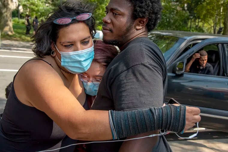 Delaney Keefe (center), a second-year Villanova law student who helped file the injunction against the city, is embraced by Josephine August (left) and Ace (right) at the encampment after learning that a federal judge ruled the City of Philadelphia can clear out the site.