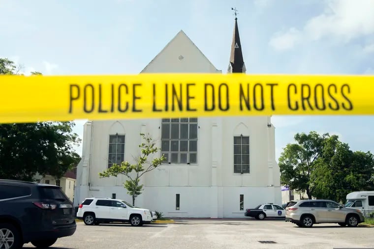 Police tape surrounded the parking lot behind the AME Emanuel Church as FBI forensic experts work the crime scene, in Charleston, S.C. Families of nine victims killed in a racist attack at the church have reached a settlement with the Justice Department over a faulty background check that allowed Dylann Roof to purchase the gun he used in the 2015 massacre.