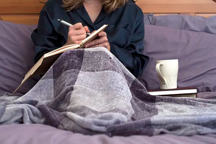 A woman journals in bed.  Cropped at woman's neck.