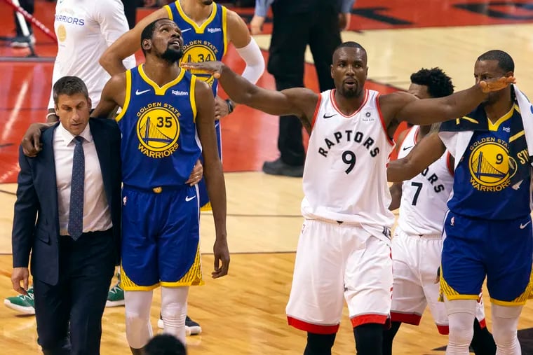 Kevin Durant (35) walks off the court after getting injured in the second quarter, as Raptors center Serge Ibaka (9) attempts to quell the fans' reaction.