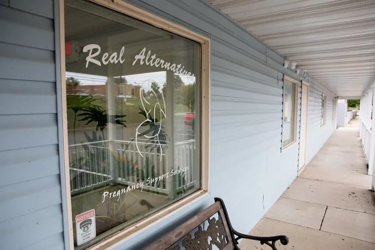 Real Alternatives, an anti-abortion organization that's received more than $100 million from the state of Pennsylvania, sits in an office plaza Harrisburg, near a thrift store and a pizza shop and across from an elementary school, visible in the reflection.