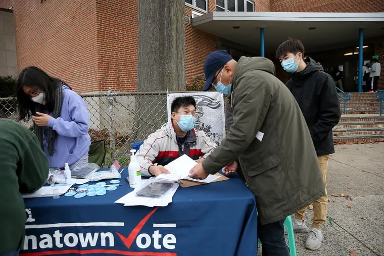 Wei Chen, center, of Asian Americans United, helps Jimmy Huang, right, of Northeast Philadelphia, at an early in-person mail voting location at the J. Hampton Moore School in Philadelphia on Oct. 25.