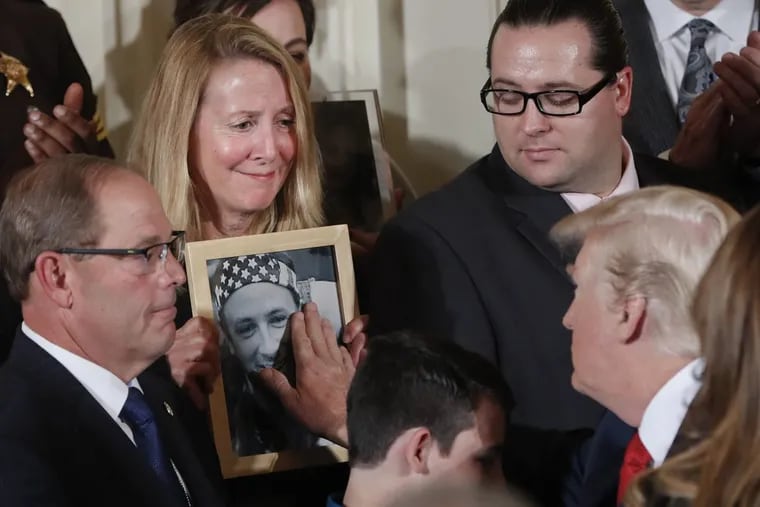 Jeanne Moser of New Hampshire watches as President Trump reaches out to touch a photo of her son Adam Moser during a ceremony on combating the opioid crisis at the White House. Adam Moser was 27 when he died from an apparent fentanyl overdose.