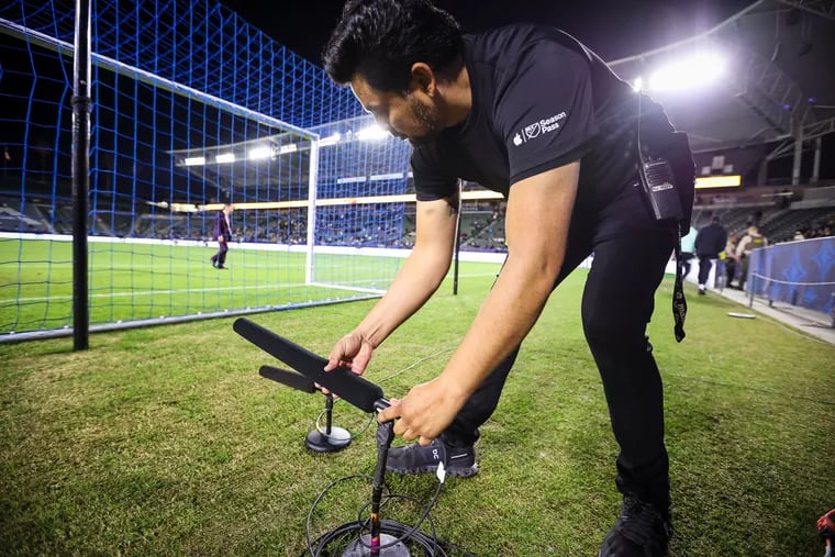 A sound technician from the Apple MLS Season Pass production staff working with a microphone on the field before a Los Angeles Galaxy vs. New York City FC preseason game.