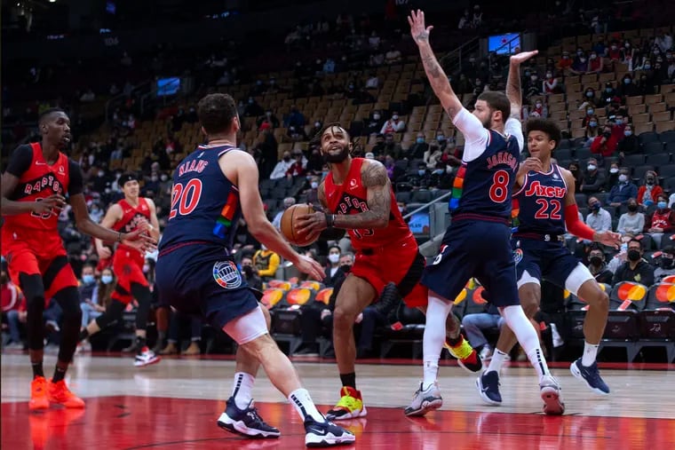 The Toronto Raptors' Gary Trent Jr. (center) looks to shoot between Sixers replacement player Tyler Johnson and Georges Niang.