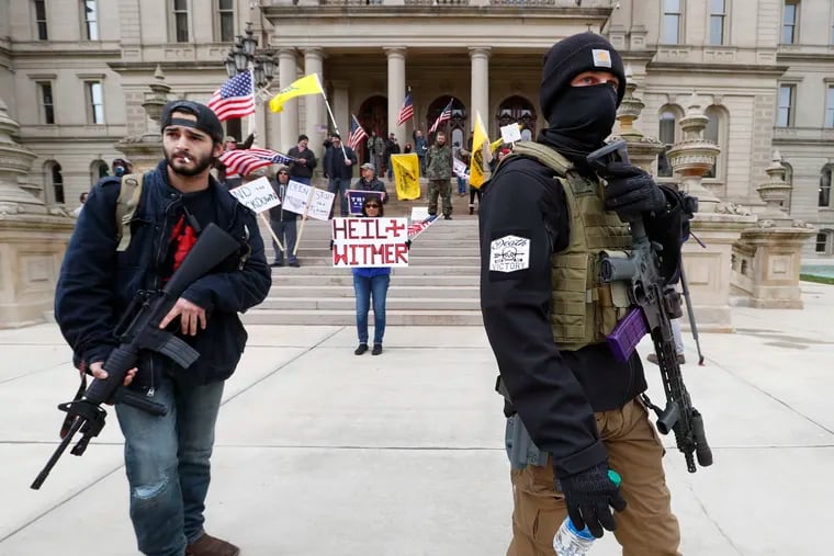 In this April 15 photo, protesters carry rifles near the steps of the Michigan State Capitol building in Lansing, Mich.