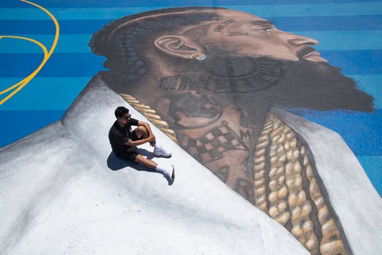 In this April 17, 2019, photo, mural artist Gustavo Zermeno Jr. poses for photos on a basketball court mural he dedicated to slain rapper Nipsey Hussle in Los Angeles. More than 50 colorful murals of Hussle have popped up in Los Angeles since the beloved rapper and community activist was gunned down outside his clothing store.