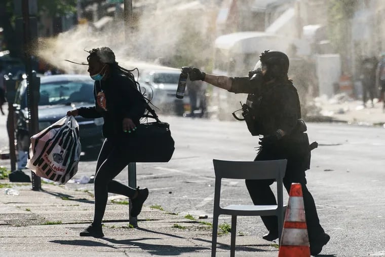 A person runs through a cloud of tear gas while being sprayed with a chemical by police after a large crowd near the the foot locker was dispersed by police at 52nd and Chestnut Streets, May 31, 2020.