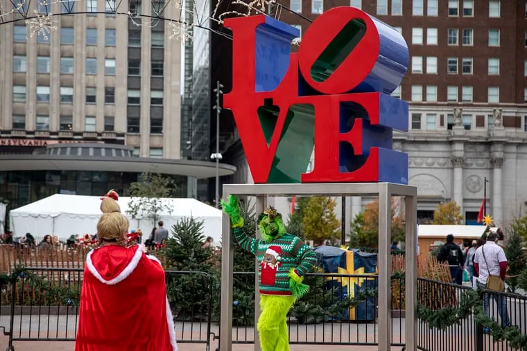 Julio Perez Eright, of York County, Pa., poses with the LOVE Park statue as Mandy McLaughlin takes the photo at the Christmas Village on Saturday. The two have been dressing up as the Grinch and Cindy Lou Who for a few years and are visiting for the first time.