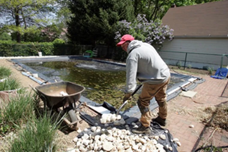 John Cashman, 35, shovels decorative stones around a pool in Princeton Junction. Unemployed, he was hired by a friend to landscape his yard. (Barbara L. Johnston / Inquirer)