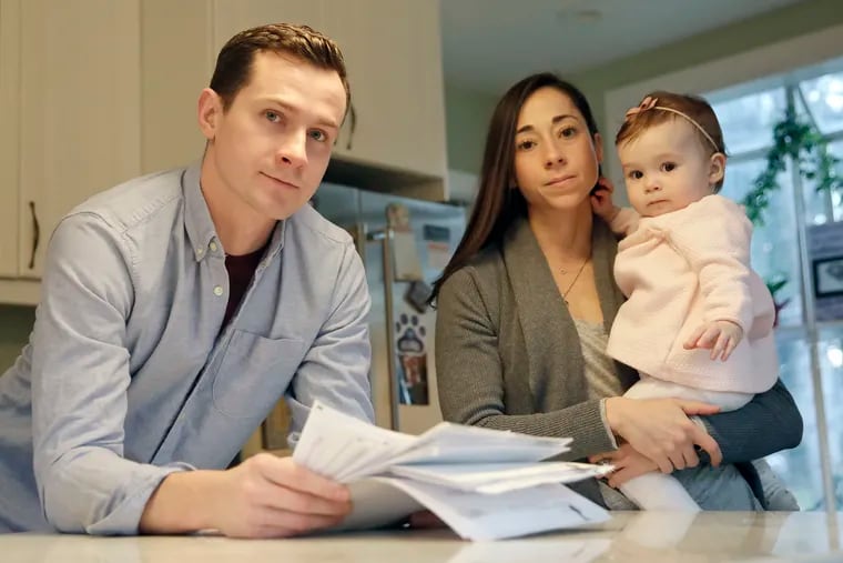 Alex and Jodi Laughlin with their 10-month-old daughter Lily in their Riverton, NJ home. Alex is holding medical bills from the birth of their first daughter Noelle who lived just 32 minutes after a pre-term emergency C-section due to health complications.