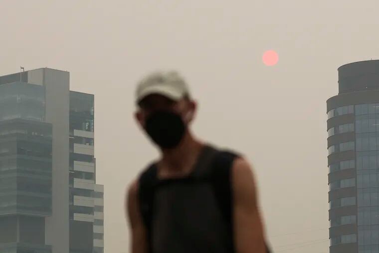 Masked pedestrians cross the South St. Bridge in Philadelphia as a hazy sun is behind them due to the wildfires in Canada on Wednesday, June 7, 2023.